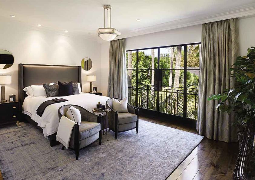 A serene sleeping room designed by Coppel Design for the Hombly Hills project, featuring a plush king-sized bed, elegant bedding, modern furniture, and large windows that offer a view of the surrounding landscape.