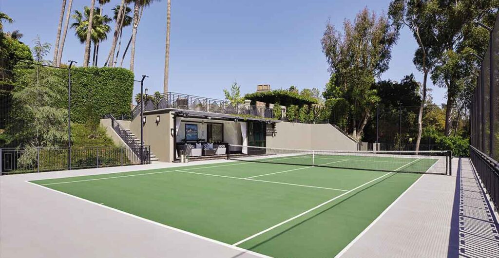 A private tennis court within the Hombly Hills project designed by Coppel Design, featuring a well-maintained playing surface surrounded by lush landscaping and modern fencing, set against a backdrop of elegant residential architecture.